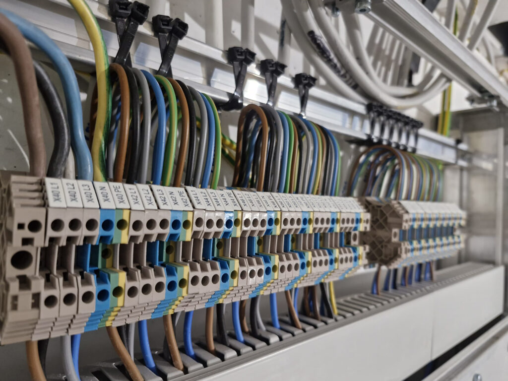 Image d'un collaborateur CEL Image de l'arrière d'un tableau électrique avec des câbles tous rangés et aligné correctement. Cette image est représentative pour le contrôle périodique OIBT puisqu'il peut se révéler nécessaire de devoir remplacer le tableau électrique de certaines installations.